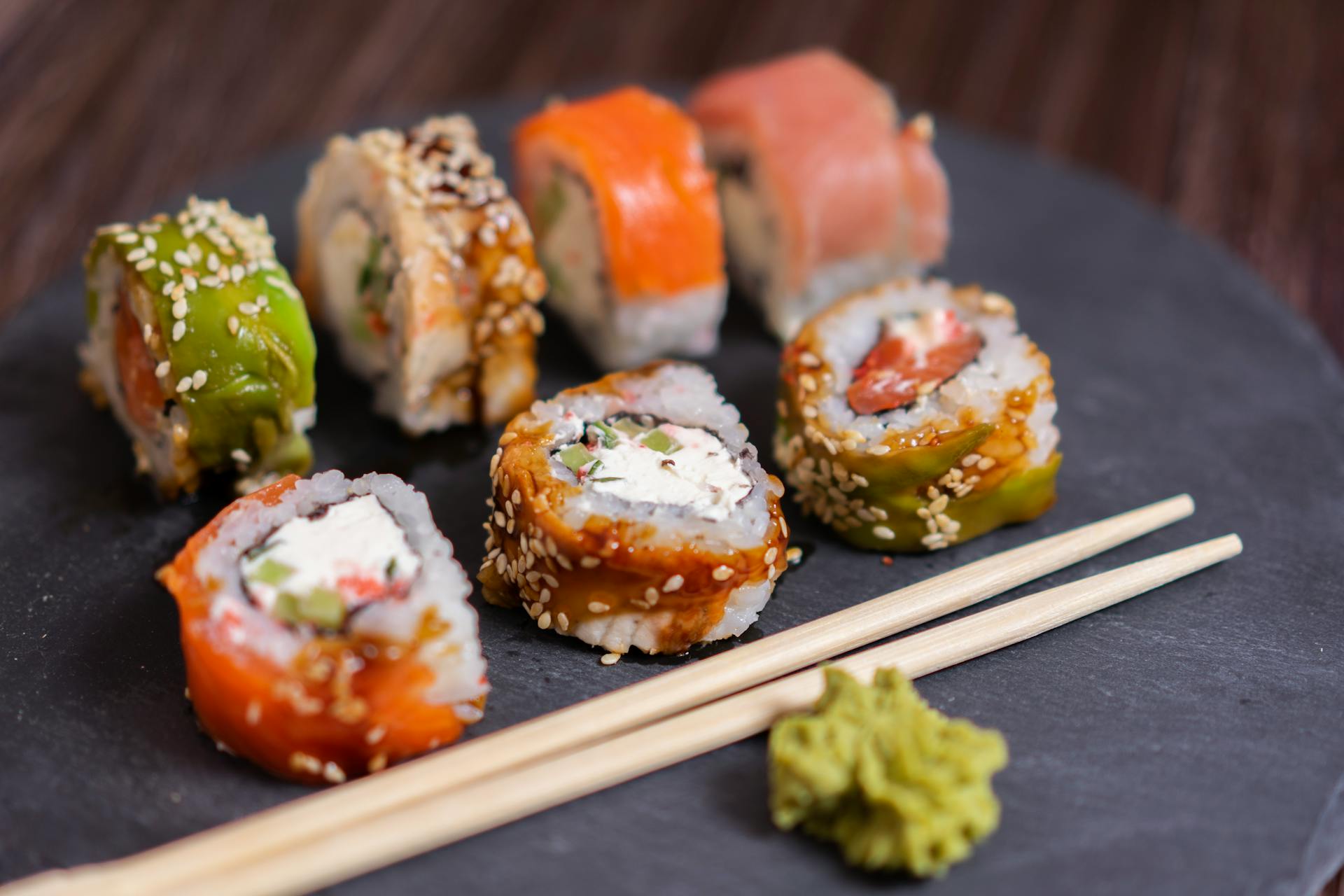 7 Stücke Sushi auf einer Schieferplatte mit Essstäbchen und Wasabi