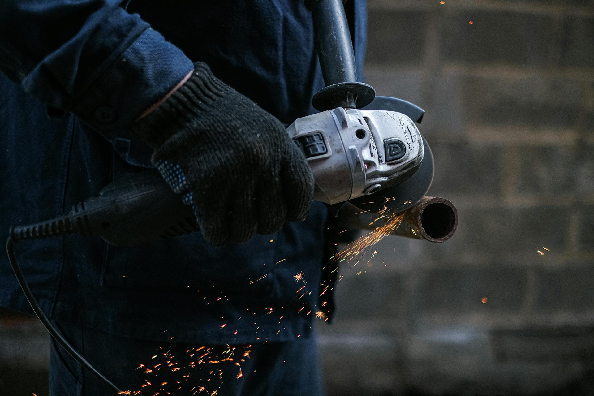 Handwerker der mit einem Winkelschleifer (Trennscheibe) ein Rohr durchtrennt.