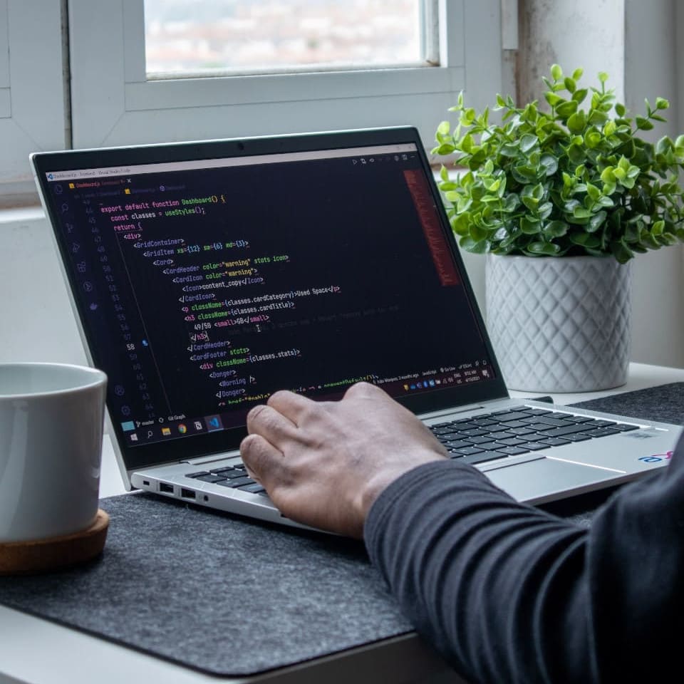 Webentwickler am Laptop mit offener IDE (VS Code) auf dem JavaScript Code einer Website zu sehen ist.