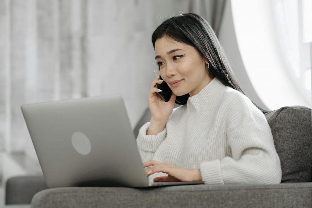 Unternehmerin die vor ihrem Laptop sitzt und dabei ĂŒber ihr Smartphone telefoniert.
