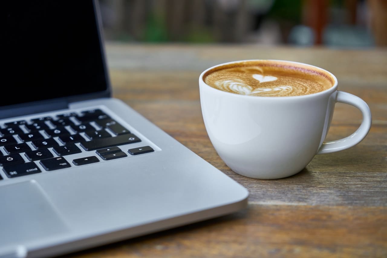 Macbook neben dem ein Café Latte steht mit ein wenig Late Art.