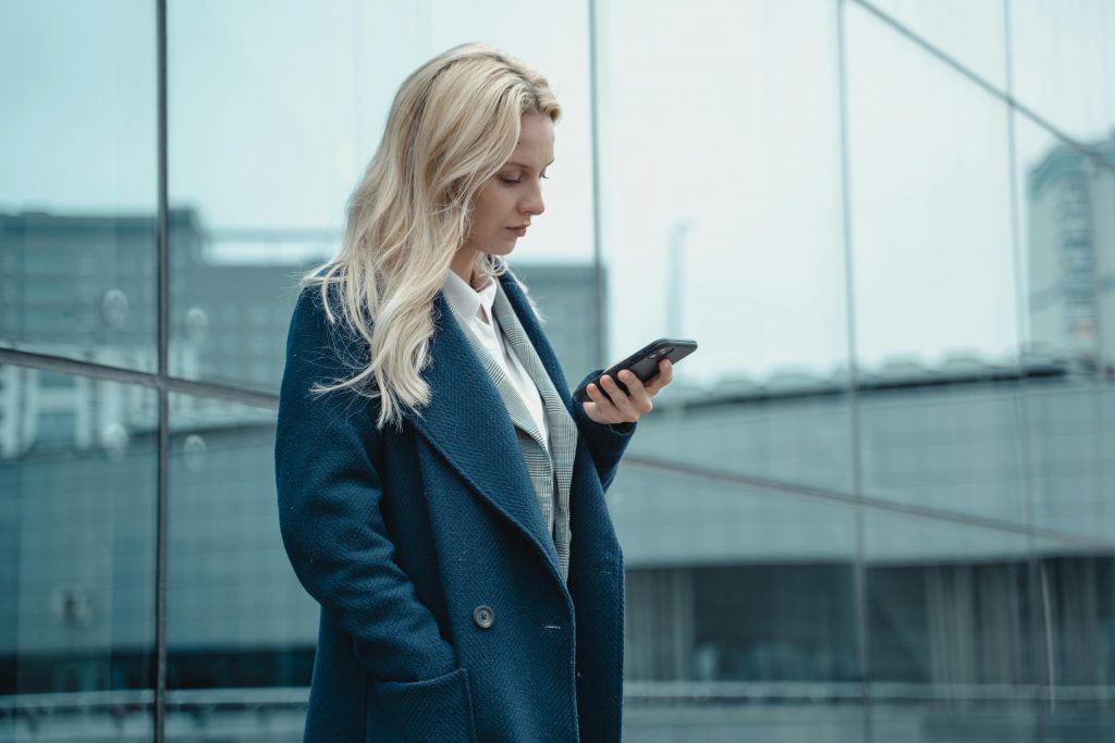 Local SEO, AI-SEO und Webdesign - Blonde Frau mit einem blauen Mantel und einem Smartphone in der Hand.